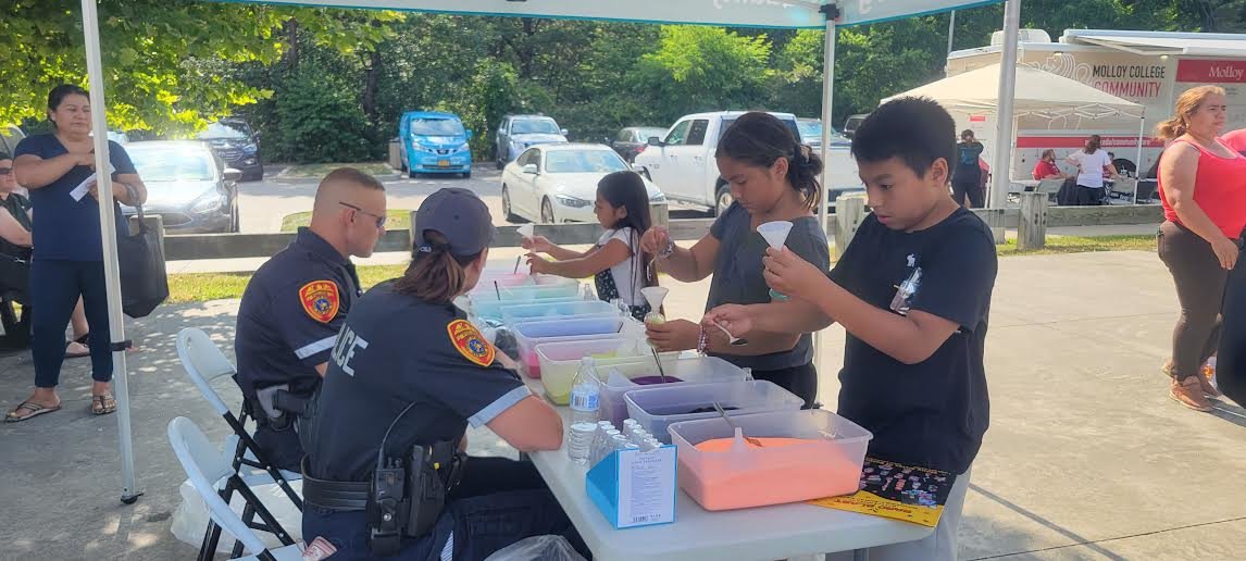 Alison (left), Camila (center) and Daniel (right) make sand art at the table run by Frank Raspanti (left) and Heidi Cummings (right) from the Seventh Precinct.